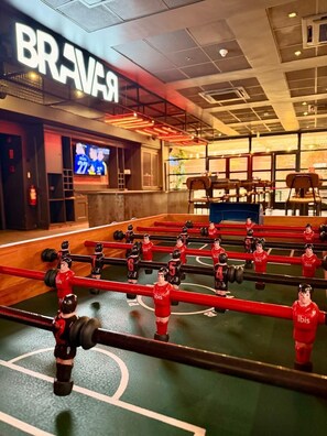 A foosball table in a room with a visible 'BRAVAR' sign, a TV screen, and a seating area with chairs. - ibis Antofagasta (Antofagasta)