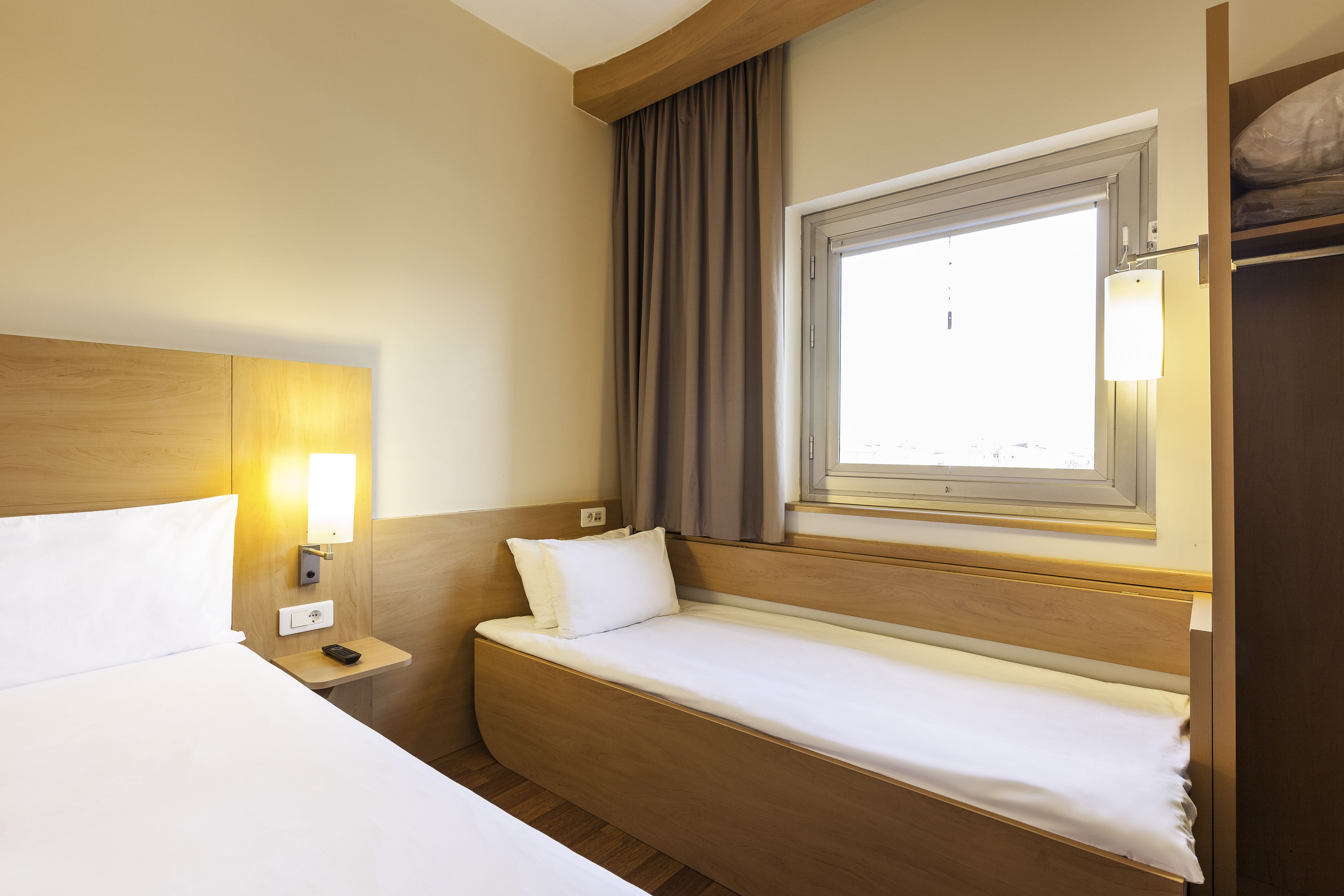 A hotel room with a bed, bedside table, lamp, window, and curtains.