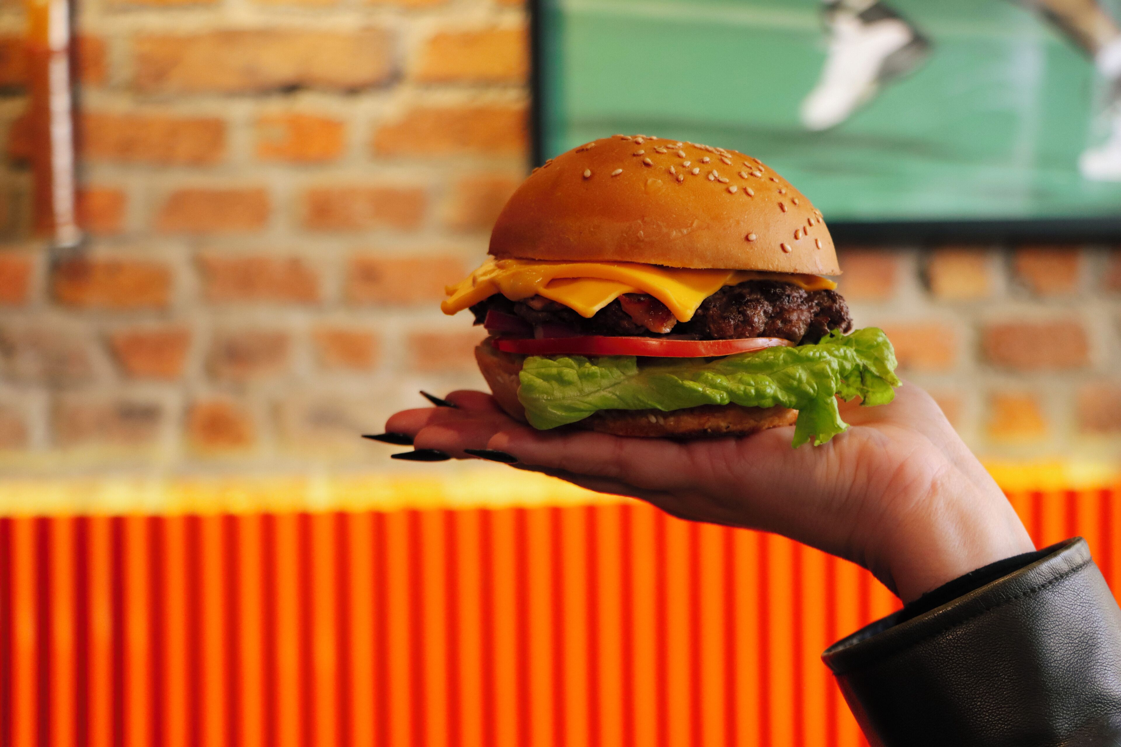 Una mano sosteniendo una hamburguesa con capas visibles de lechuga, tomate, queso y una hamburguesa de carne.