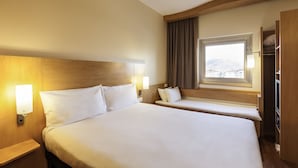 Une chambre d’hôtel avec un grand lit, des tables de chevet, une fenêtre avec des rideaux et une armoire.
