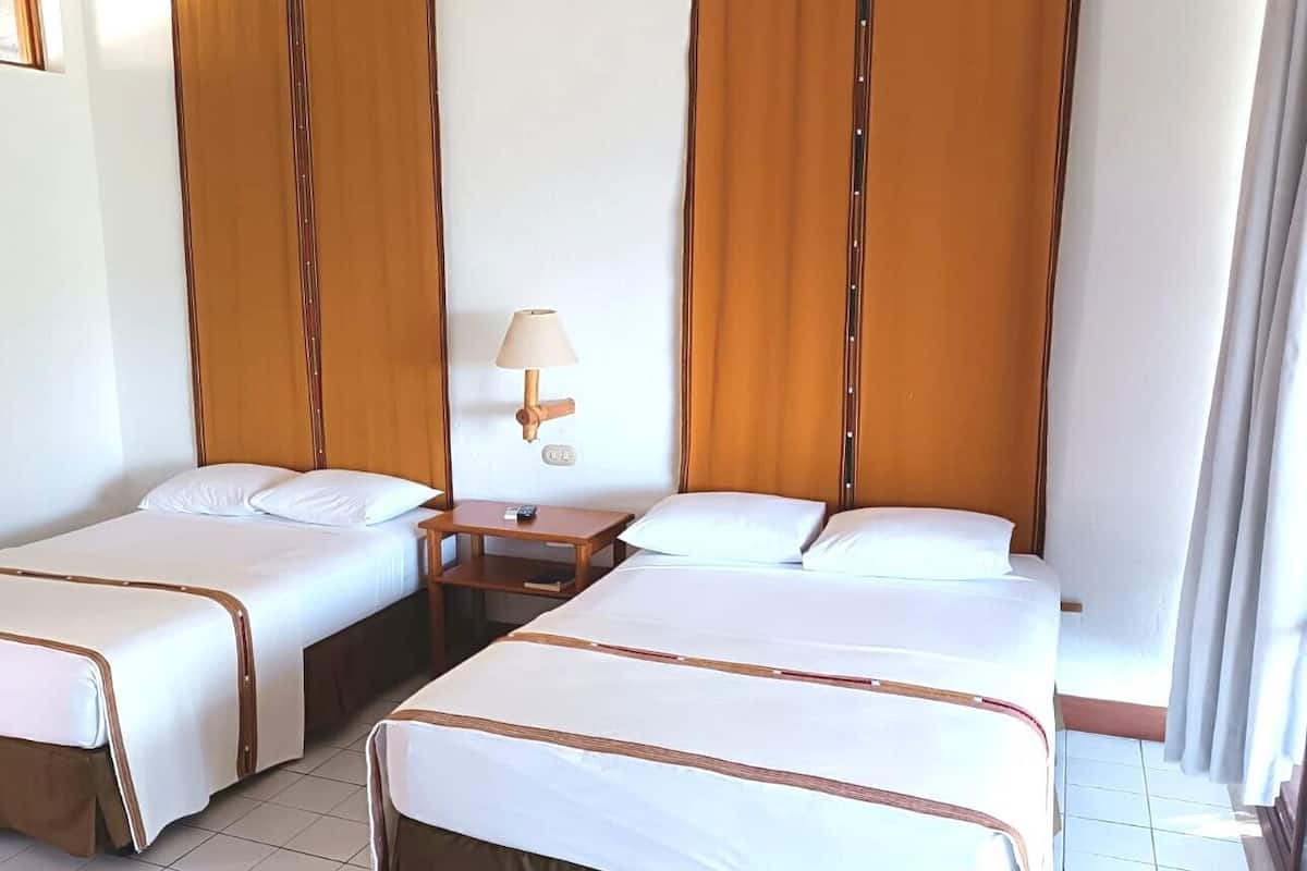 A hotel room with two beds, a nightstand, a lamp, and curtains.