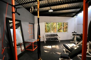 A gym with exercise equipment, a bench, a rack of dumbbells, and a window with a view of greenery.