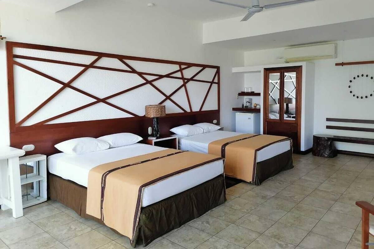 A hotel room with two beds, a desk, a chair, a ceiling fan, and a window with a view.