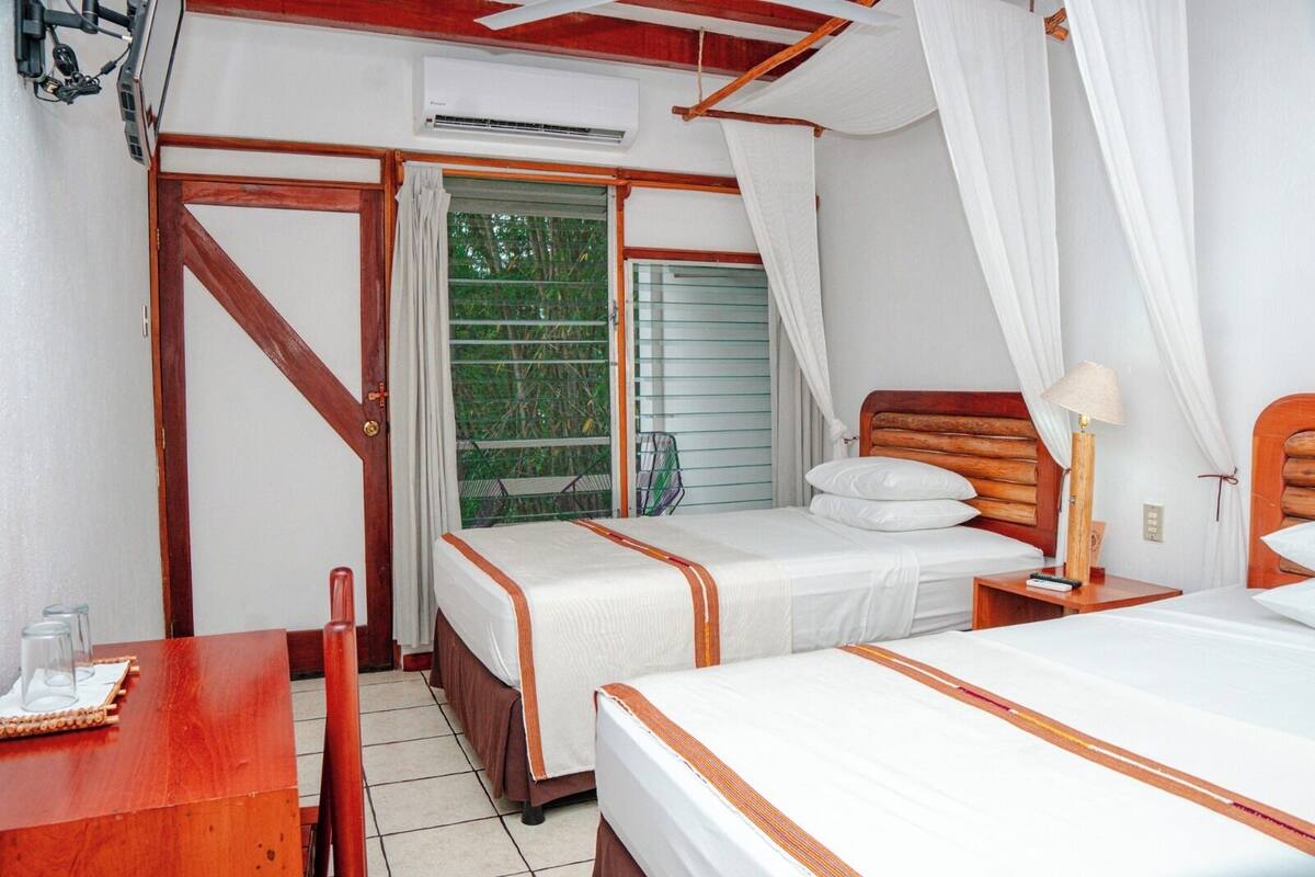 A bedroom with two beds, a wooden desk, a chair, and a window with curtains.