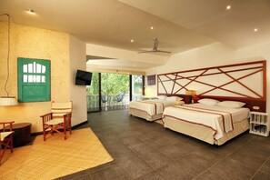 A hotel room with two beds, a TV, a balcony with chairs, and a ceiling fan.