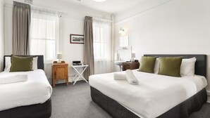 A hotel room with two beds, a small table, a chair, a mirror, and a window with curtains. - The Grand View Hotel (Wentworth Falls)