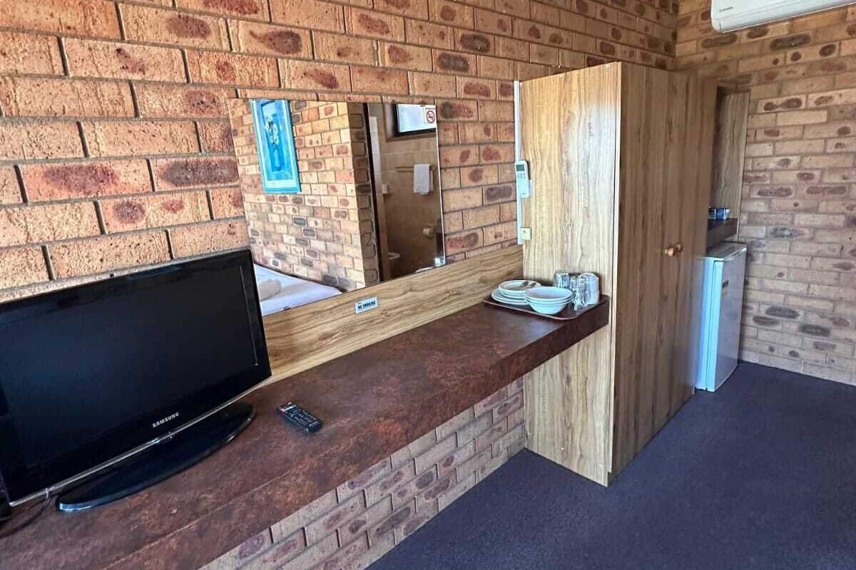 A reception area with a brick wall, a flat-screen TV, a counter with a mirror, and a door leading to another room.