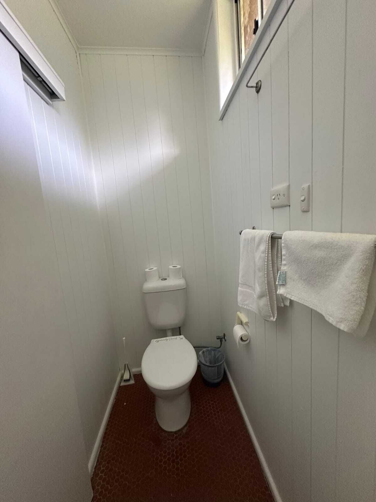 A small, narrow bathroom with white walls, a white toilet, and a single roll of toilet paper.
