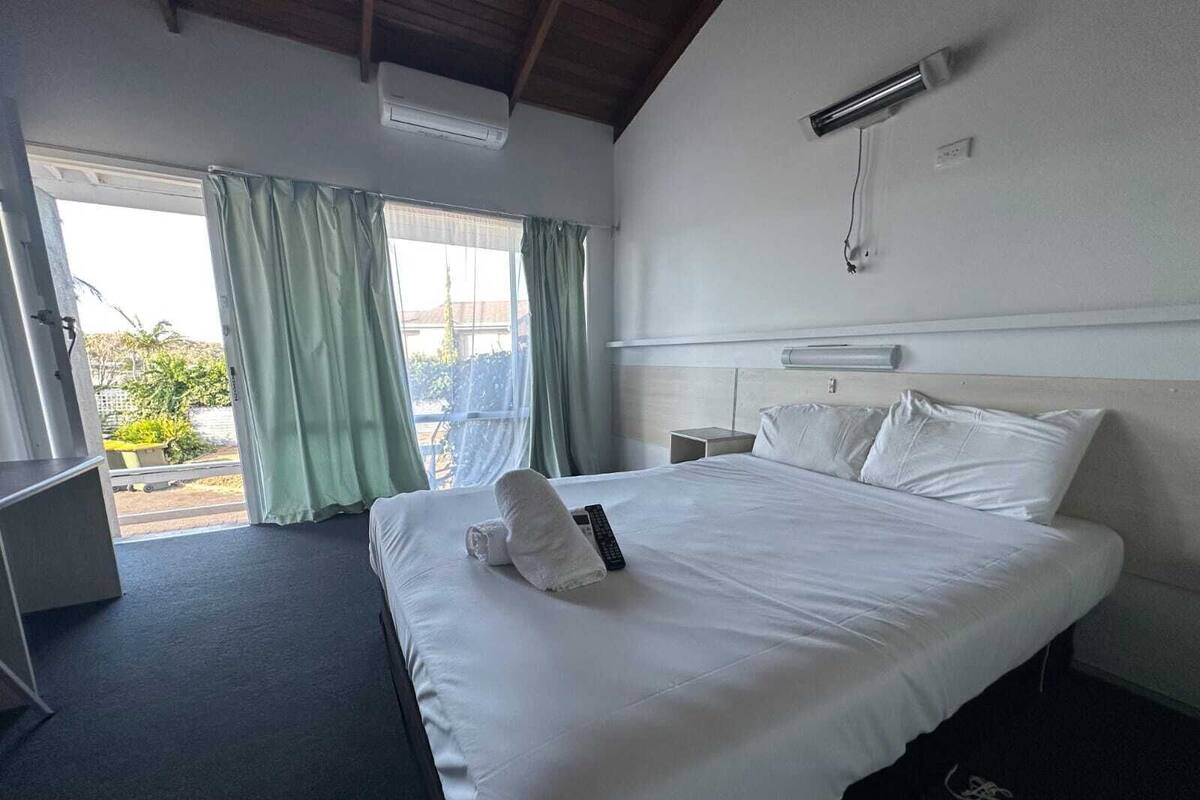 A hotel room with a large bed, a desk, and a window with curtains.