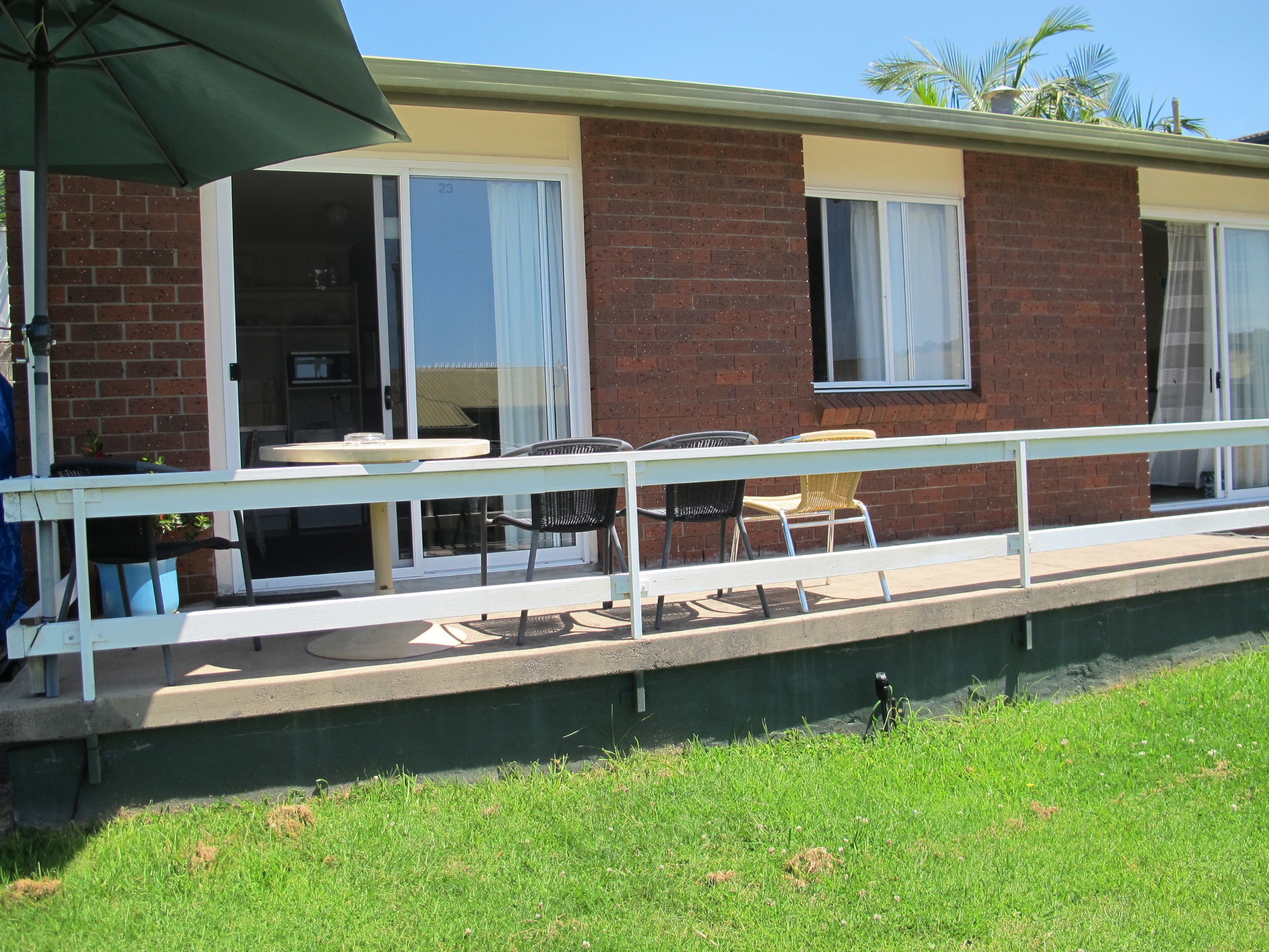 Un espace patio avec une table et des chaises, un parasol vert et un bâtiment en briques doté de grandes fenêtres.