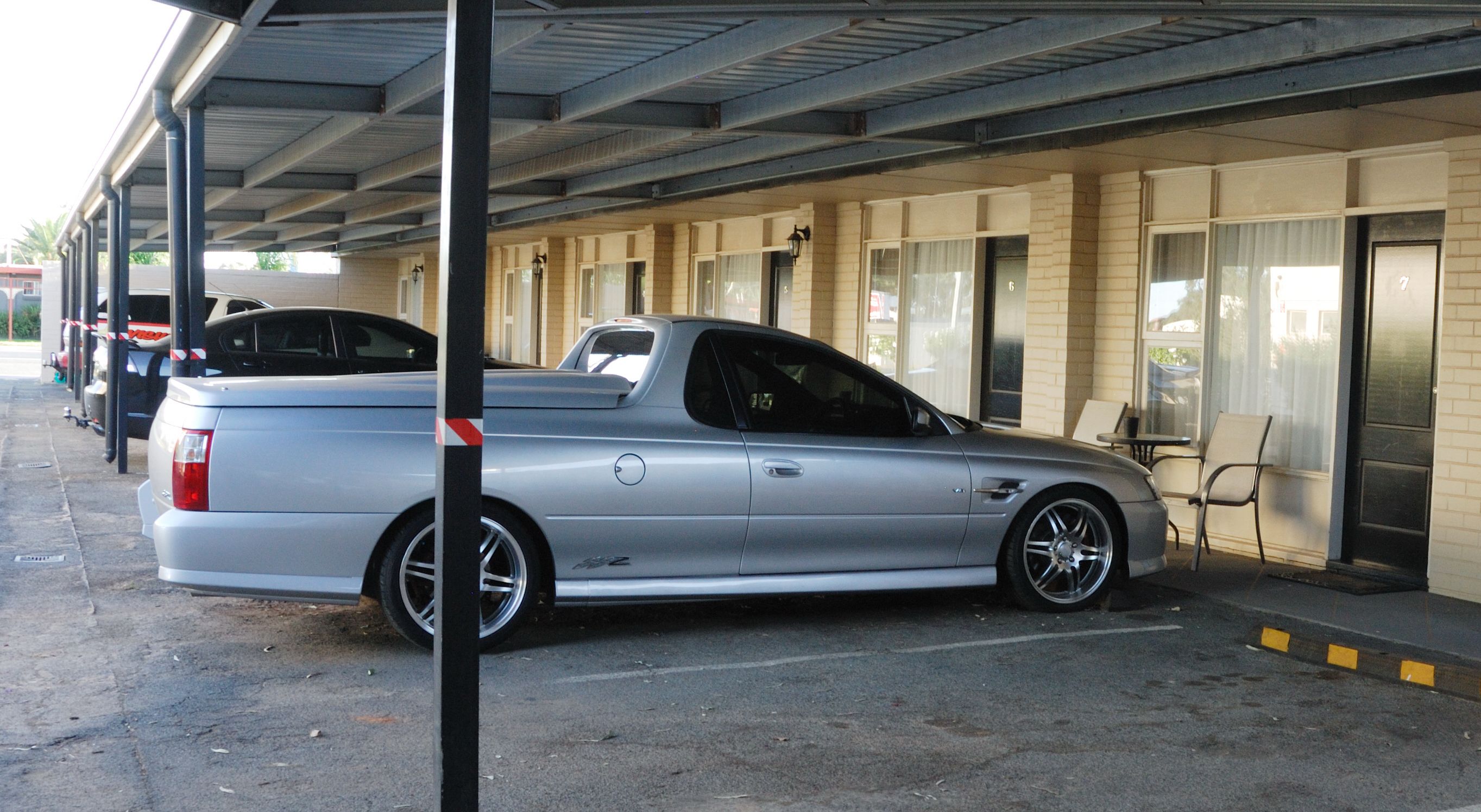 A parking area with a silver car parked under a covered structure.