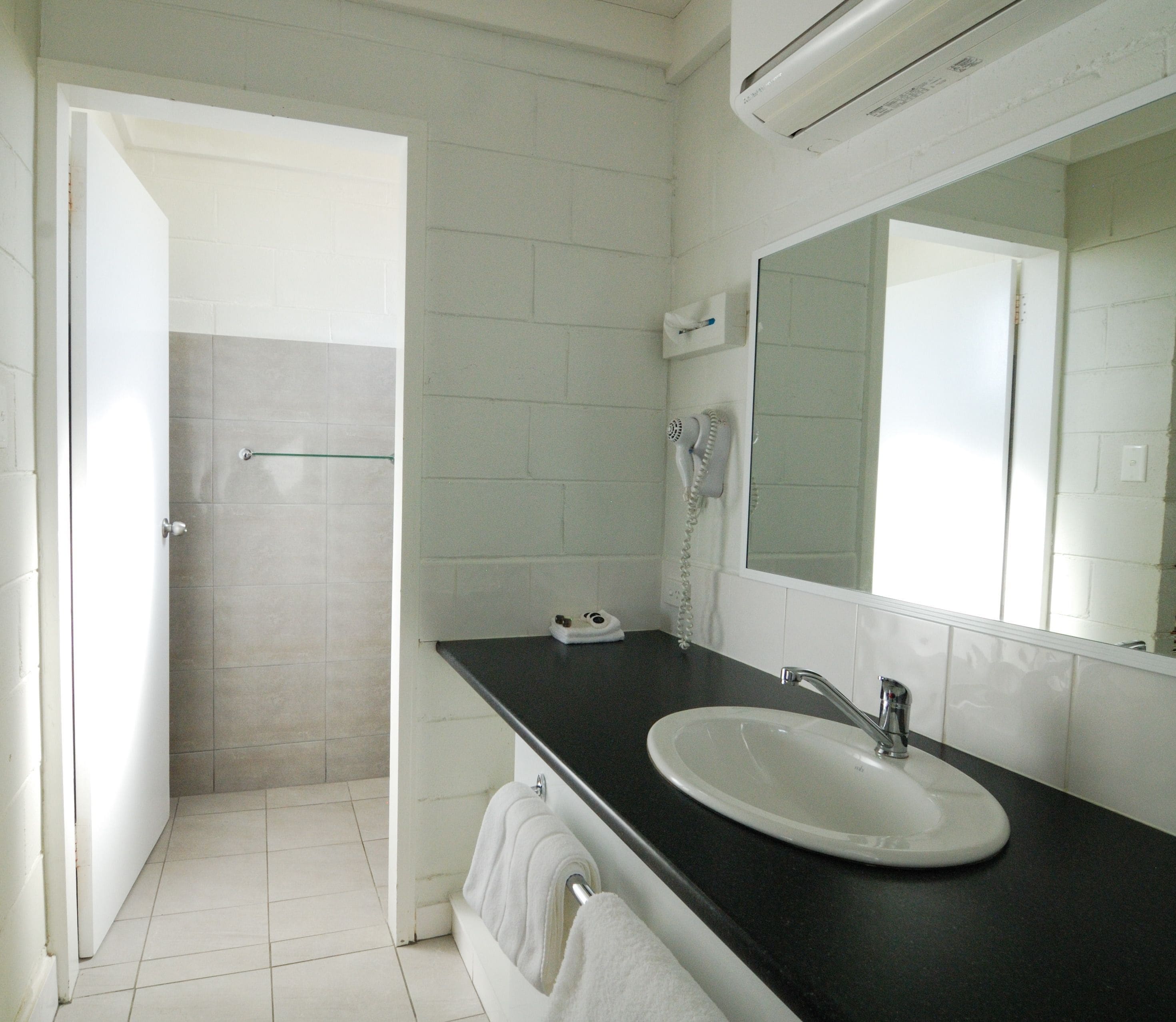 Casa de banho com lavatório branco, espelho, secador de cabelo e porta-toalhas.