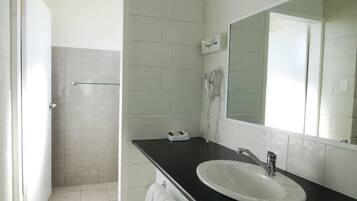 Casa de banho com lavatório branco, espelho, secador de cabelo e porta-toalhas.