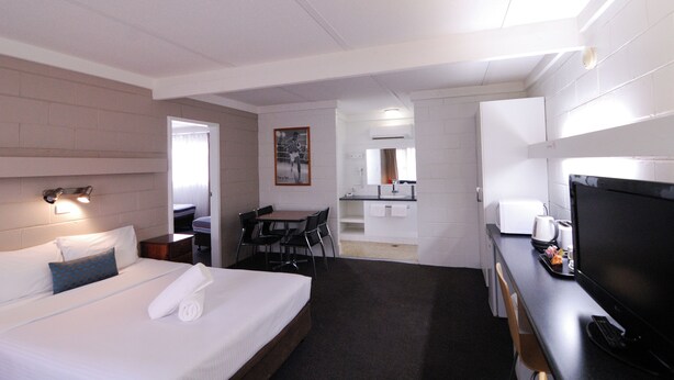 A hotel room with a bed, a desk with a computer, a TV, and a kitchenette.