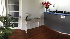 A reception desk with a blue top, a clock on the wall, and a painting depicting boats.