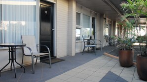 A covered outdoor seating area with tables and chairs, potted plants, and a building entrance.