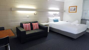 A hotel room with a black sofa, a bed, a small table, and a chair.