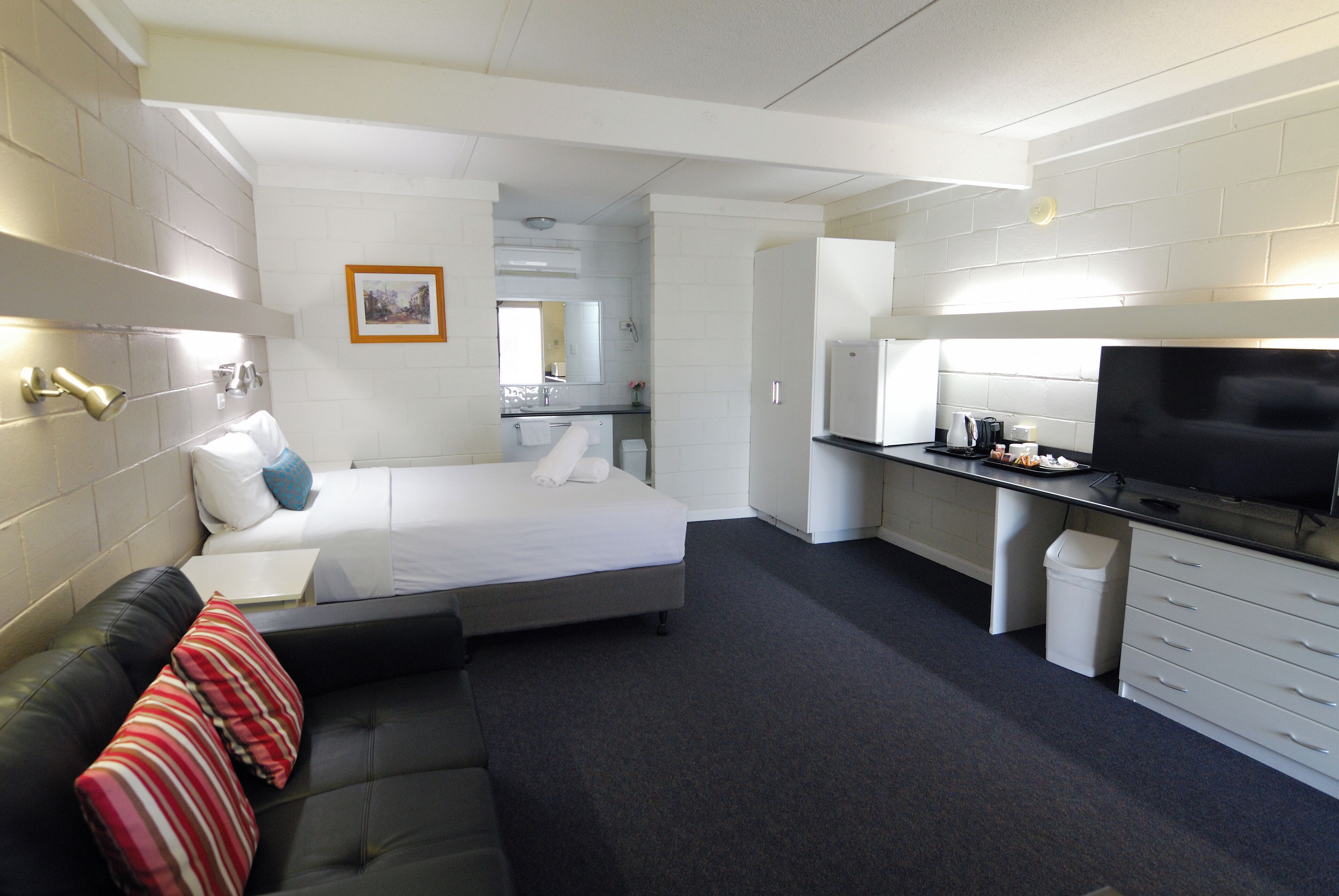 Habitación de hotel moderna con cama, sofá, televisión, una pequeña cocina y baño.