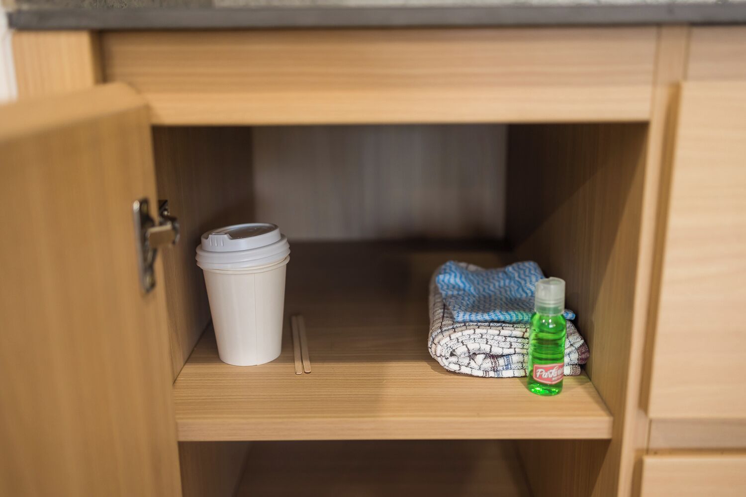 A wooden cabinet with a white cup and a bottle of hand sanitizer on the shelf.