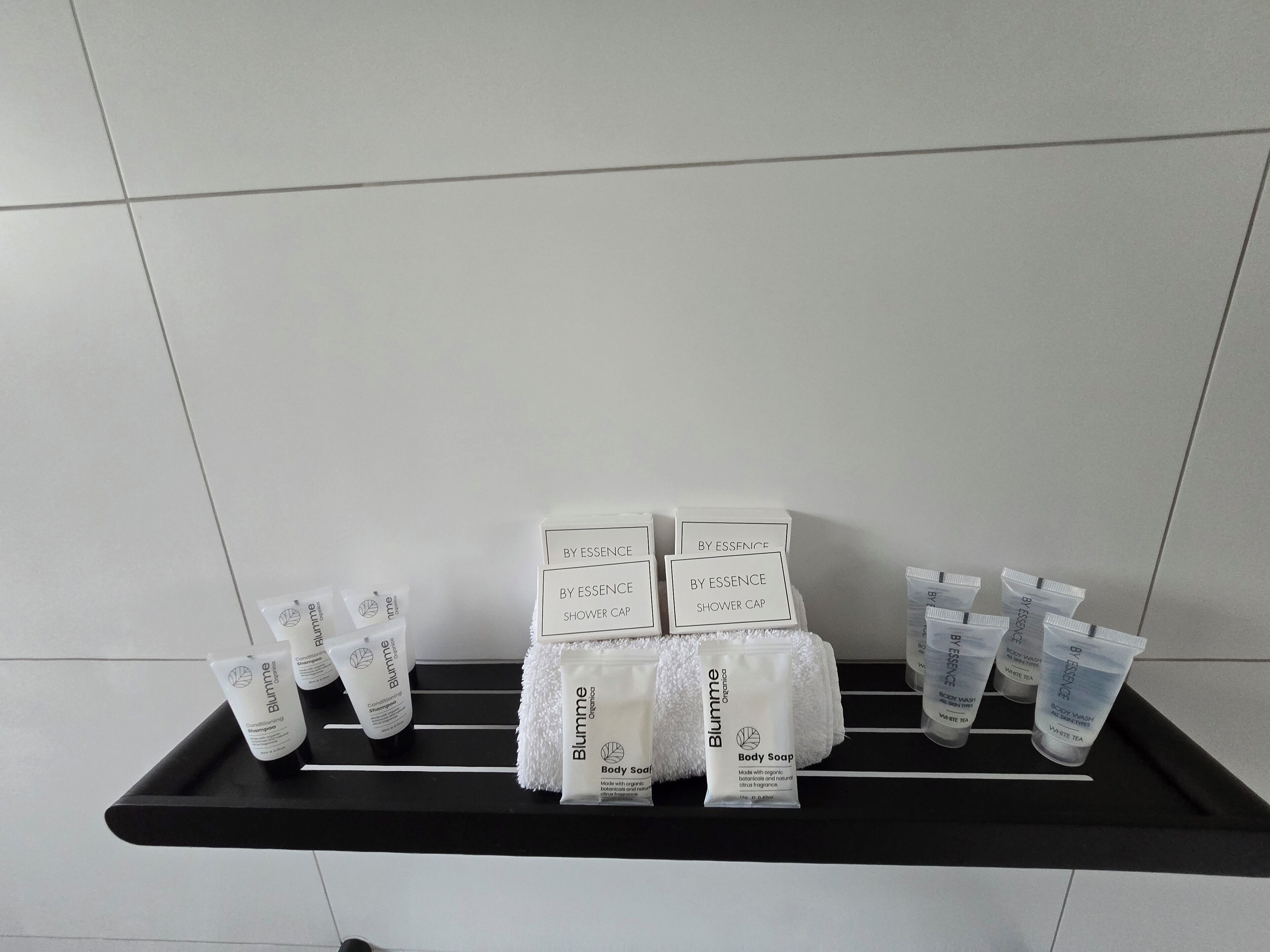 Un estante negro con diversos productos de cuidado corporal Blumme, incluyendo gorros de ducha, jabón corporal y champú.
