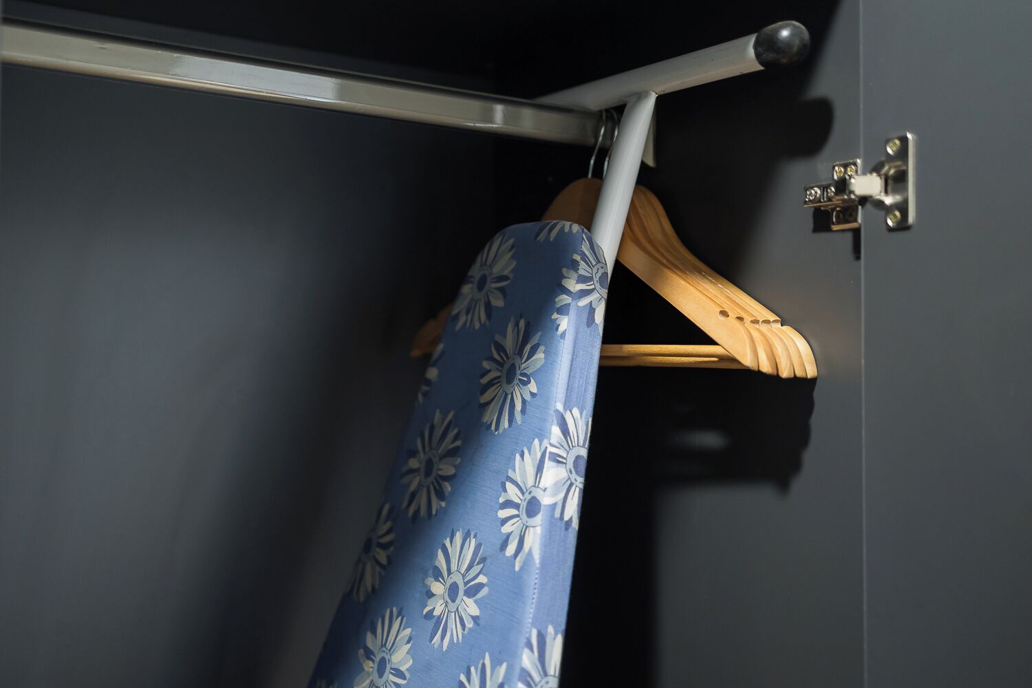 Un coin de pièce avec un cintre en bois et une planche à repasser bleue ornée d’un motif floral.