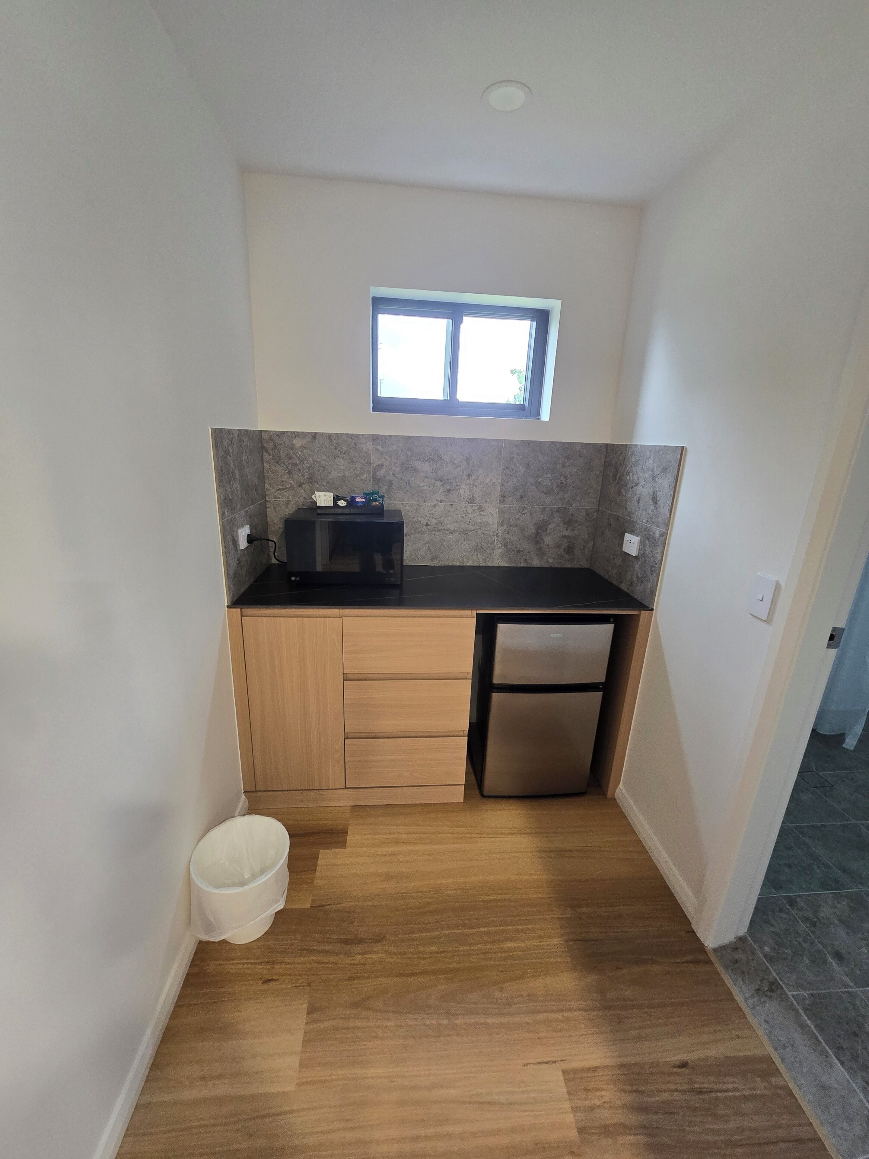 Eine kompakte Küche mit schwarzem Arbeitsplatz, Holzschränken, einem eingebauten Backofen und einem kleinen Fenster über der Spüle.
