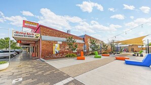 A brick building with a sign for 'Hong Loch Licensed Restaurant' and outdoor seating with colorful chairs. - Parkview Motor Inn Parkes (Parkes)