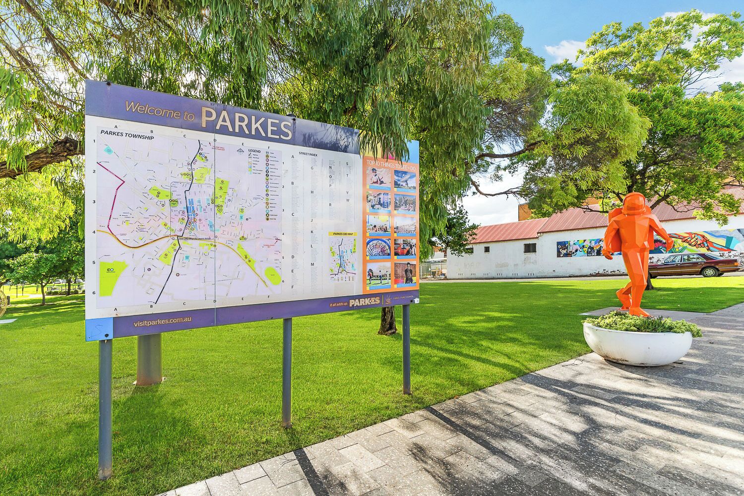 Un panneau d’accueil indiquant « PARKES », avec une carte et une statue d’une personne vêtue de vêtements orange.