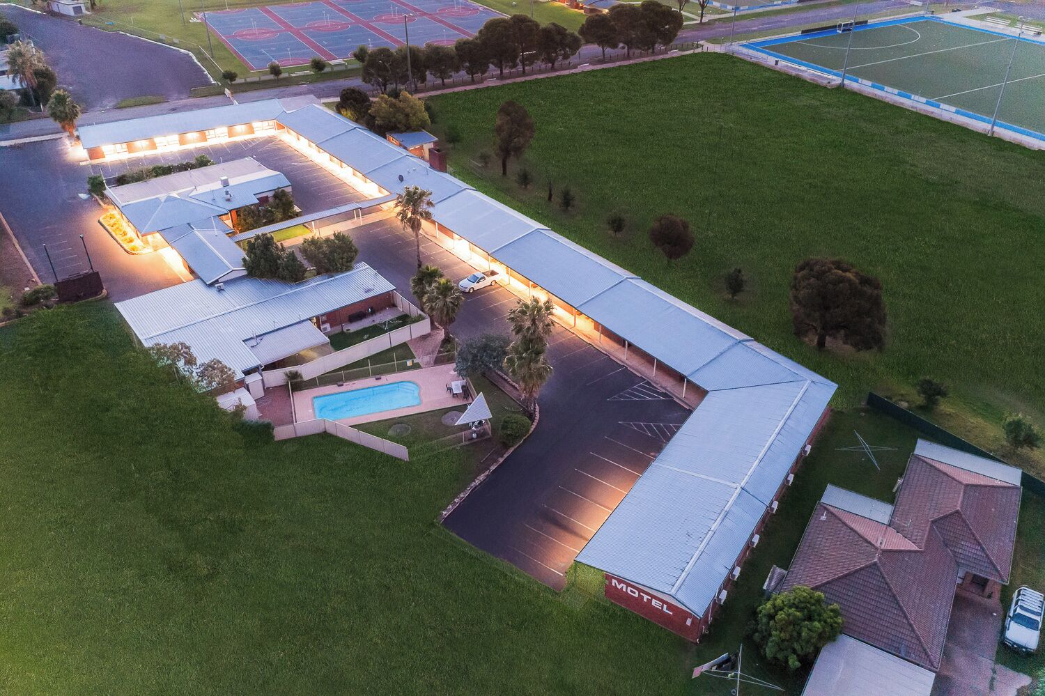 Vue aérienne d’un motel doté d’une piscine, de courts de tennis et d’un parking.