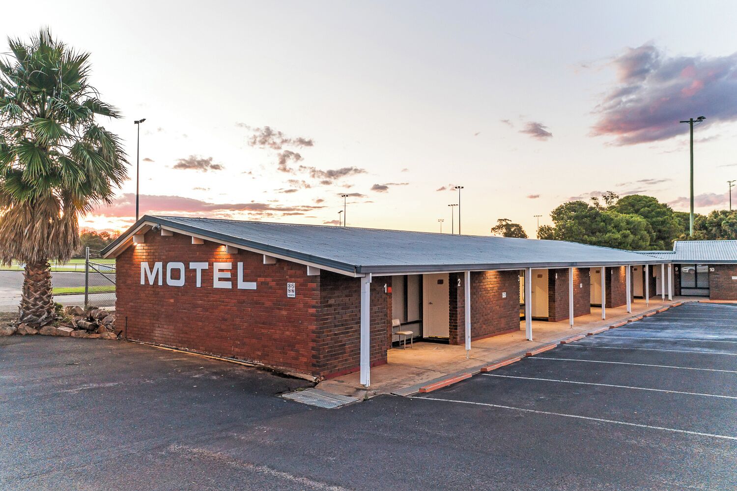 Ein Motel mit Backsteinfassade, nummerierten Zimmern und einem überdachten Parkbereich.