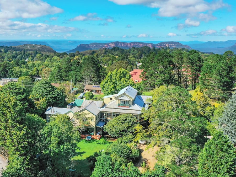 A residential area with houses surrounded by dense greenery and mountains in the background.