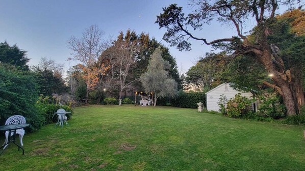 Un jardin bien entretenu, avec une pelouse, une table et des chaises de patio, entouré d’arbres et agrémenté d’un abri de jardin.