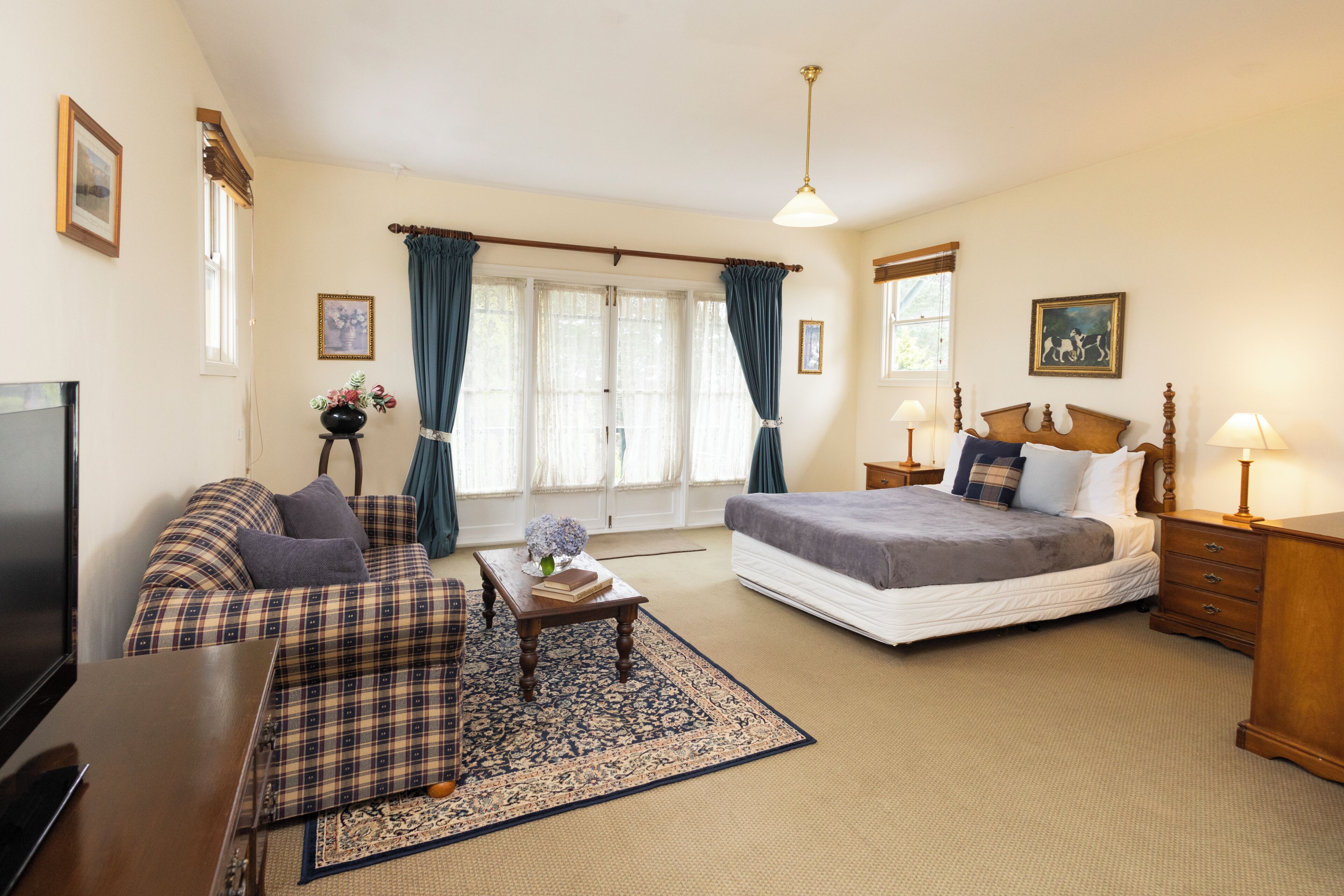 A bedroom with a bed, bedside tables, a desk, a chair, a television, and a window with curtains.