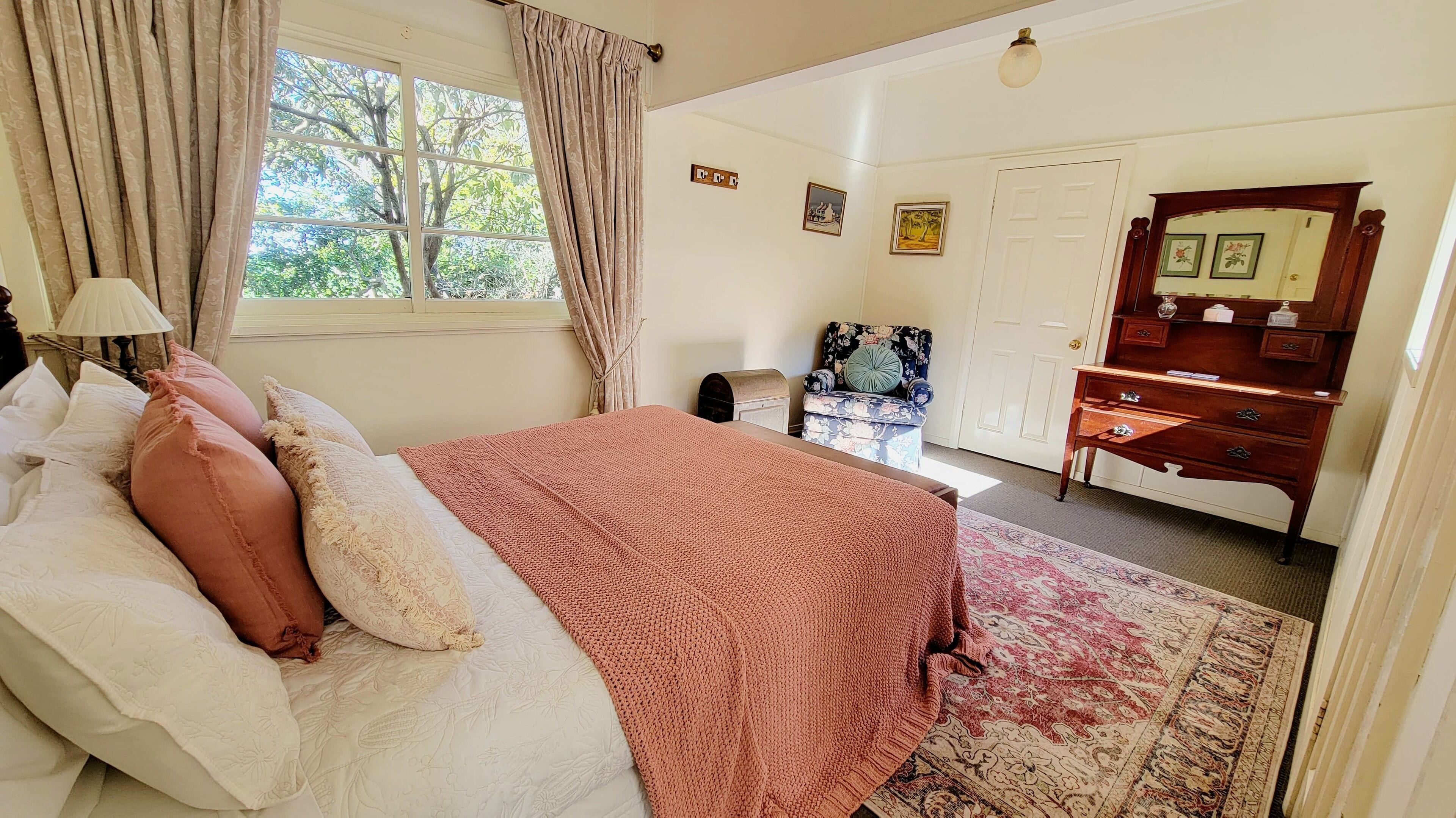 A bedroom with a bed, a dresser, a chair, and a window with curtains.
