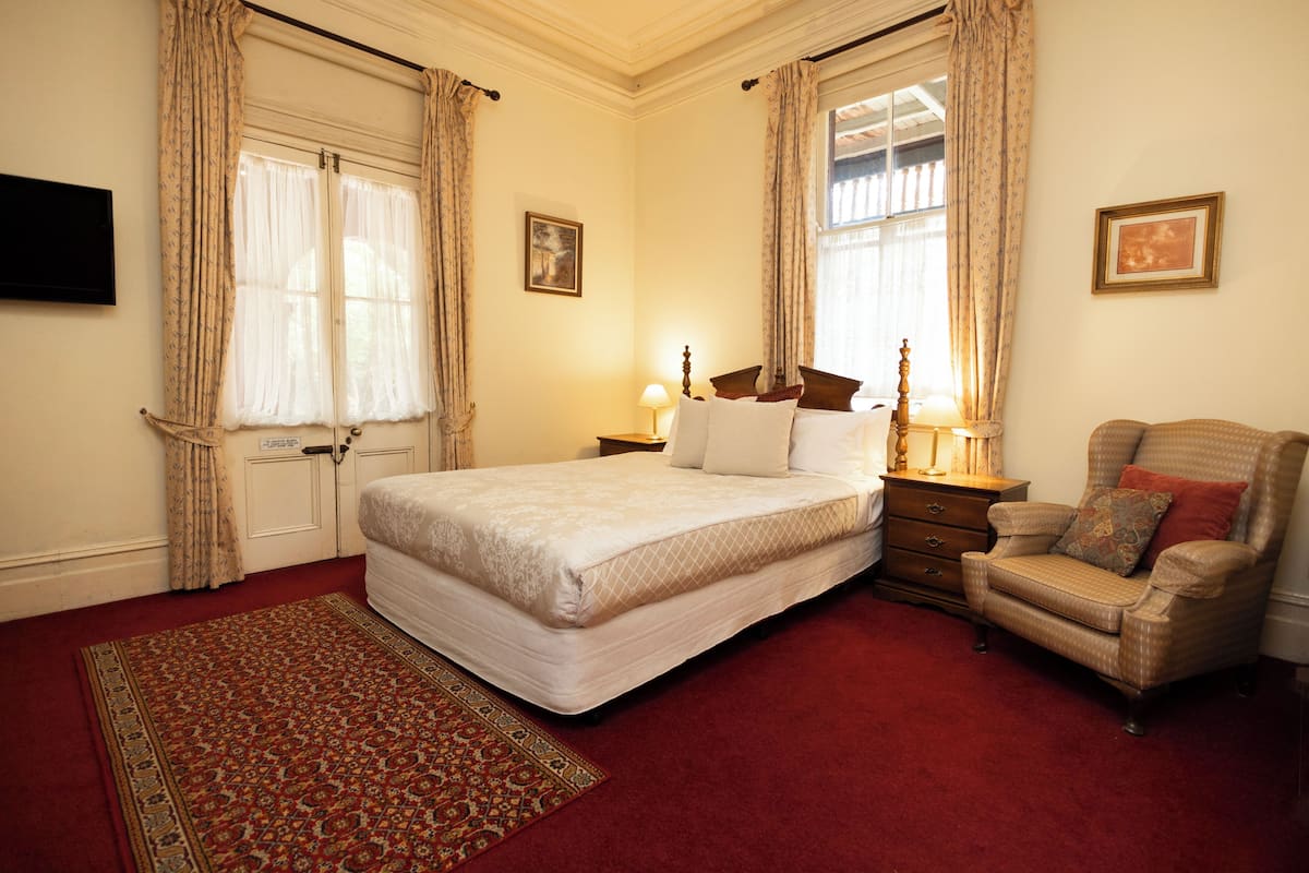 A bedroom with a large bed, a chair, a nightstand, and a window with curtains.