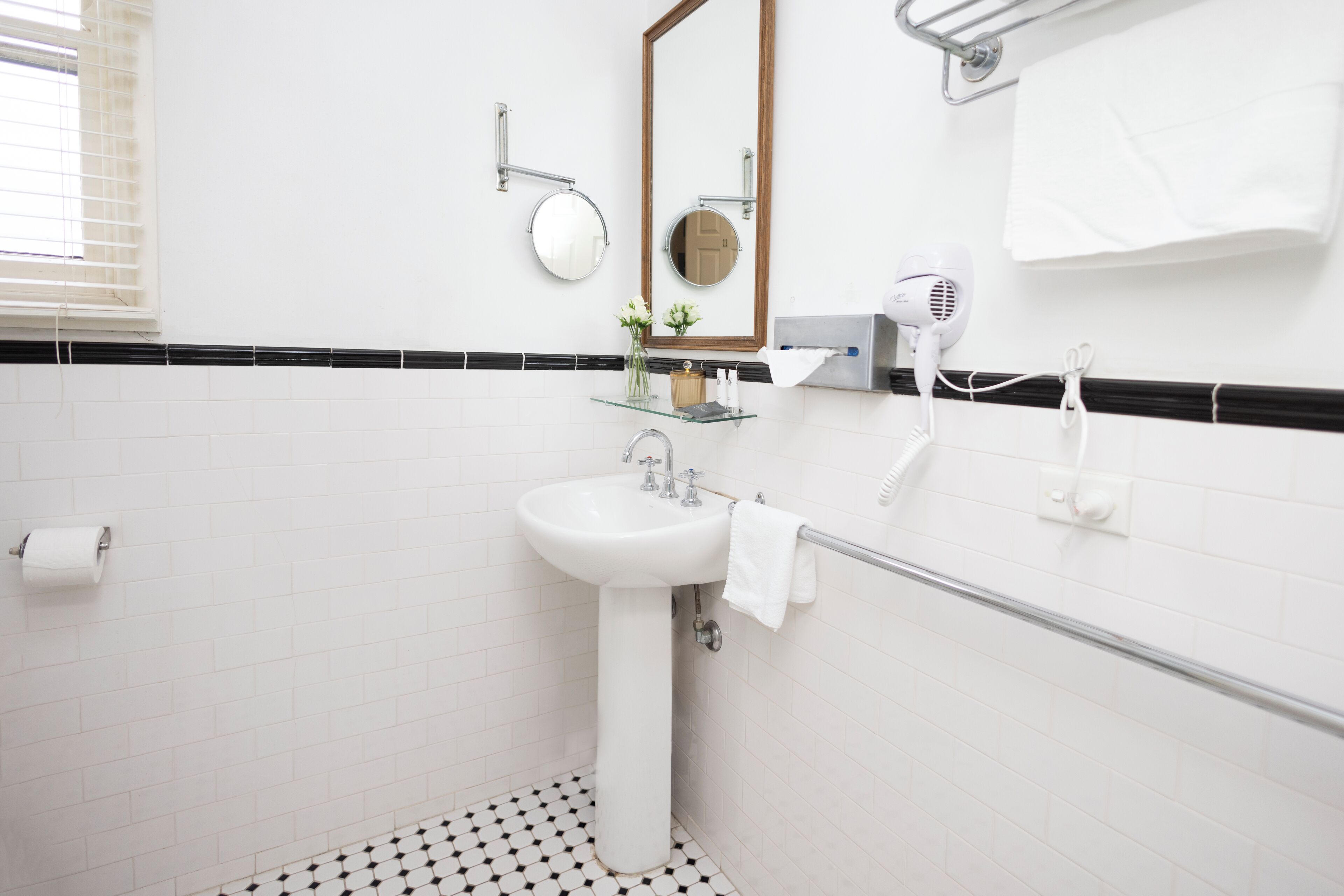 A bathroom with a white sink, mirror, towel rack, and hairdryer.