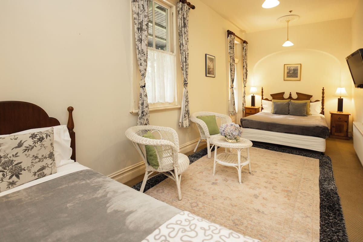 A bedroom with a bed, two chairs, a small table, a nightstand, and a television.