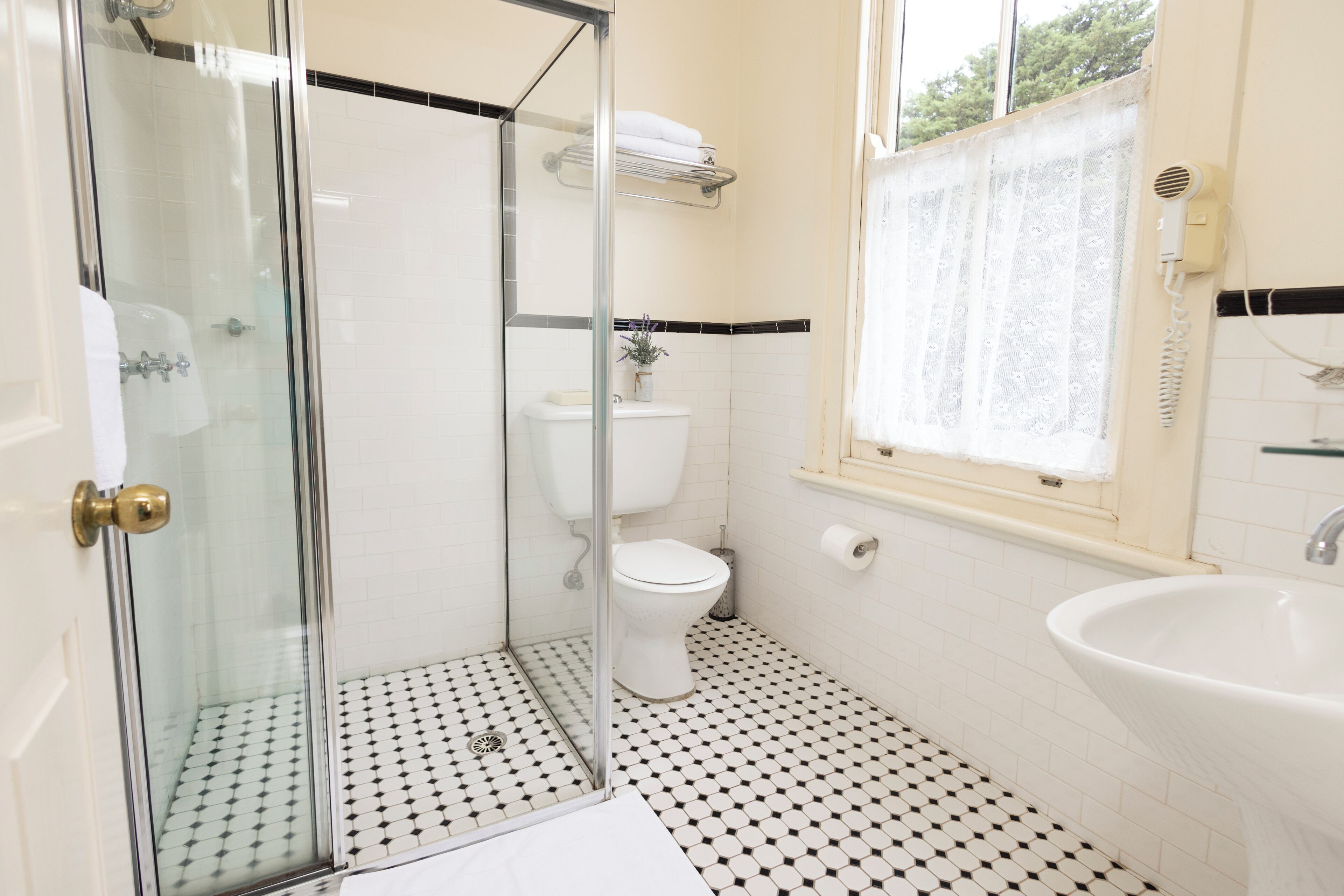 A bathroom with a glass-enclosed shower, a toilet, a sink, and a window with a showerhead.