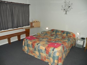 A bedroom with a bed, a desk, a chair, a lamp, and a wall decoration. - Corowa Motor Inn (Corowa)