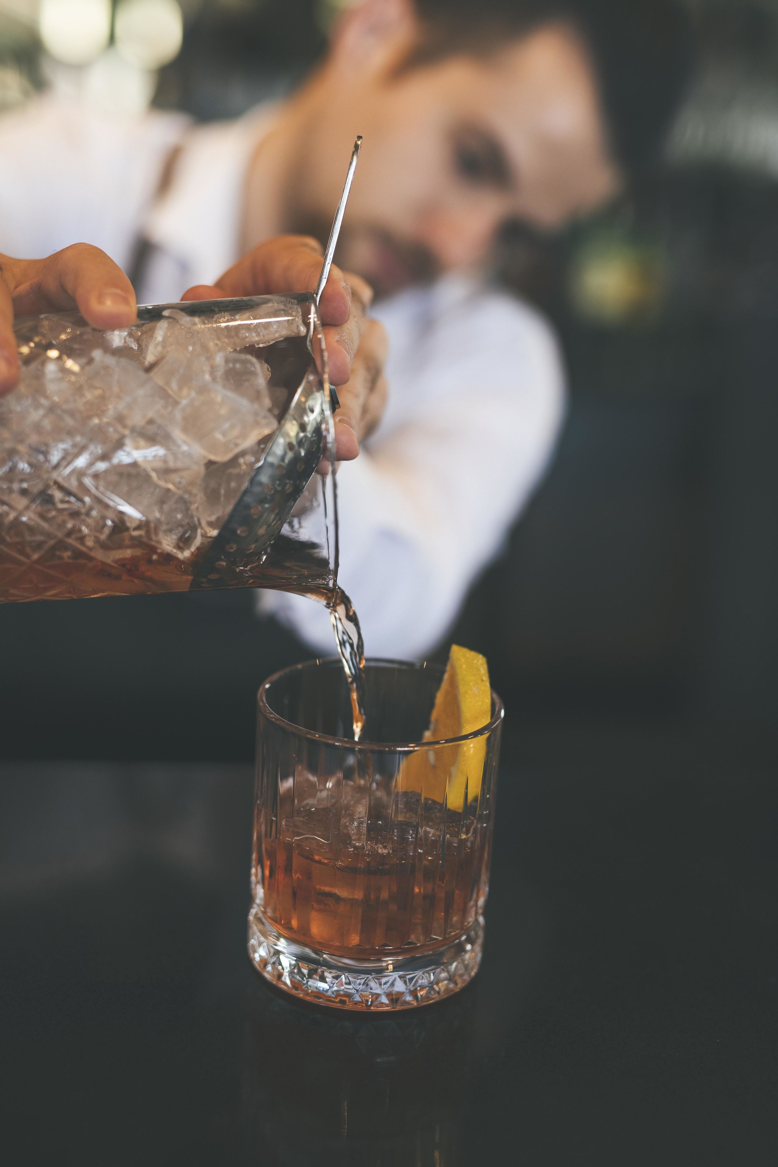 A person pouring a drink into a glass with a lemon slice.