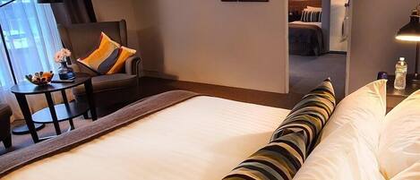 Habitación de hotel con una cama grande, un escritorio con silla, televisor montado en la pared y cuadros enmarcados.