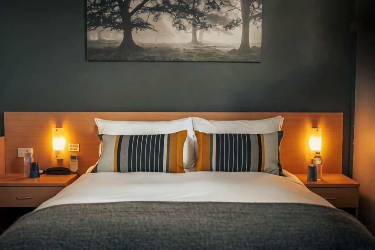 A neatly made bed with a headboard, two bedside lamps, and a wall-mounted painting.
