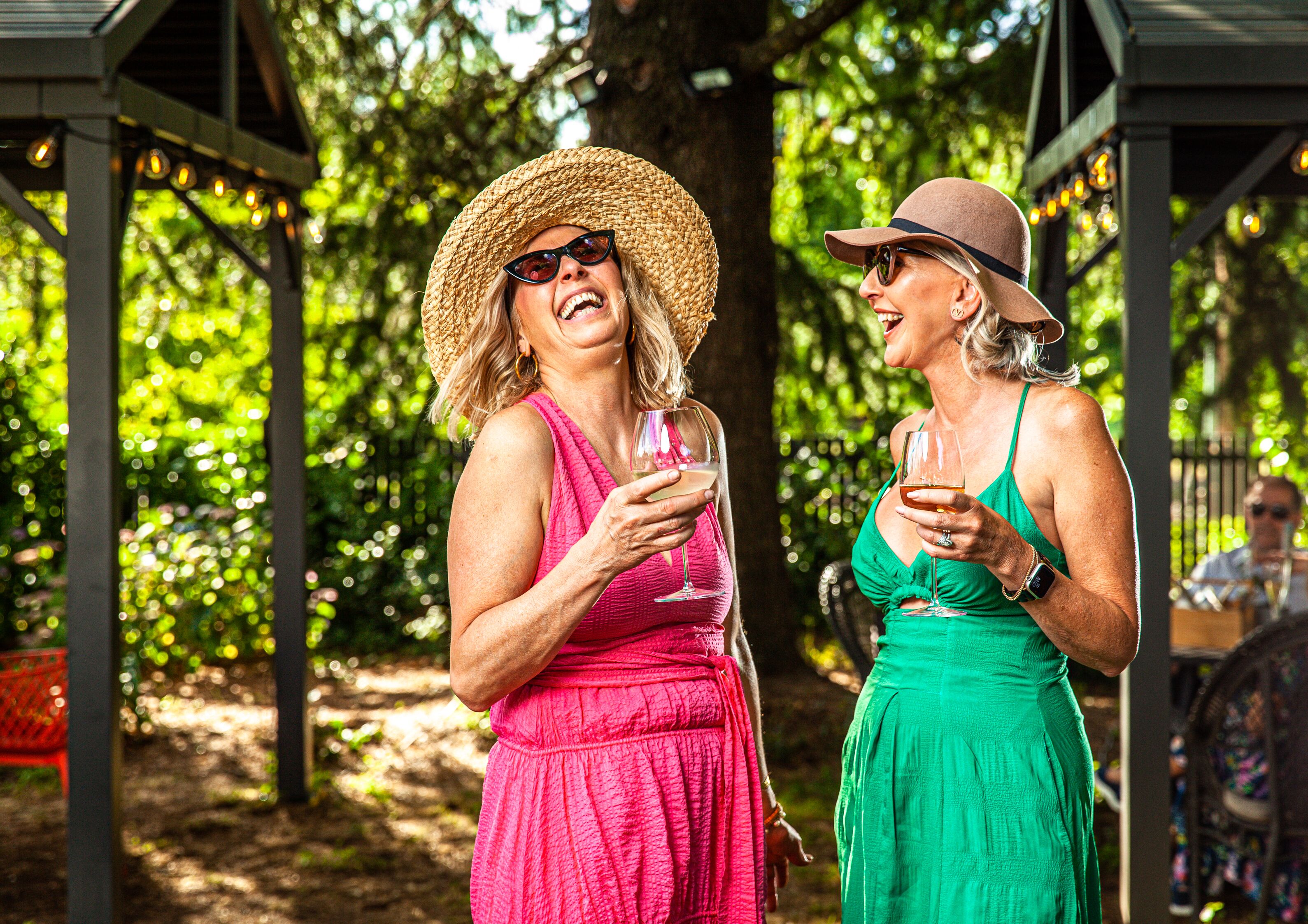 Two people standing under a gazebo with string lights, surrounded by greenery.