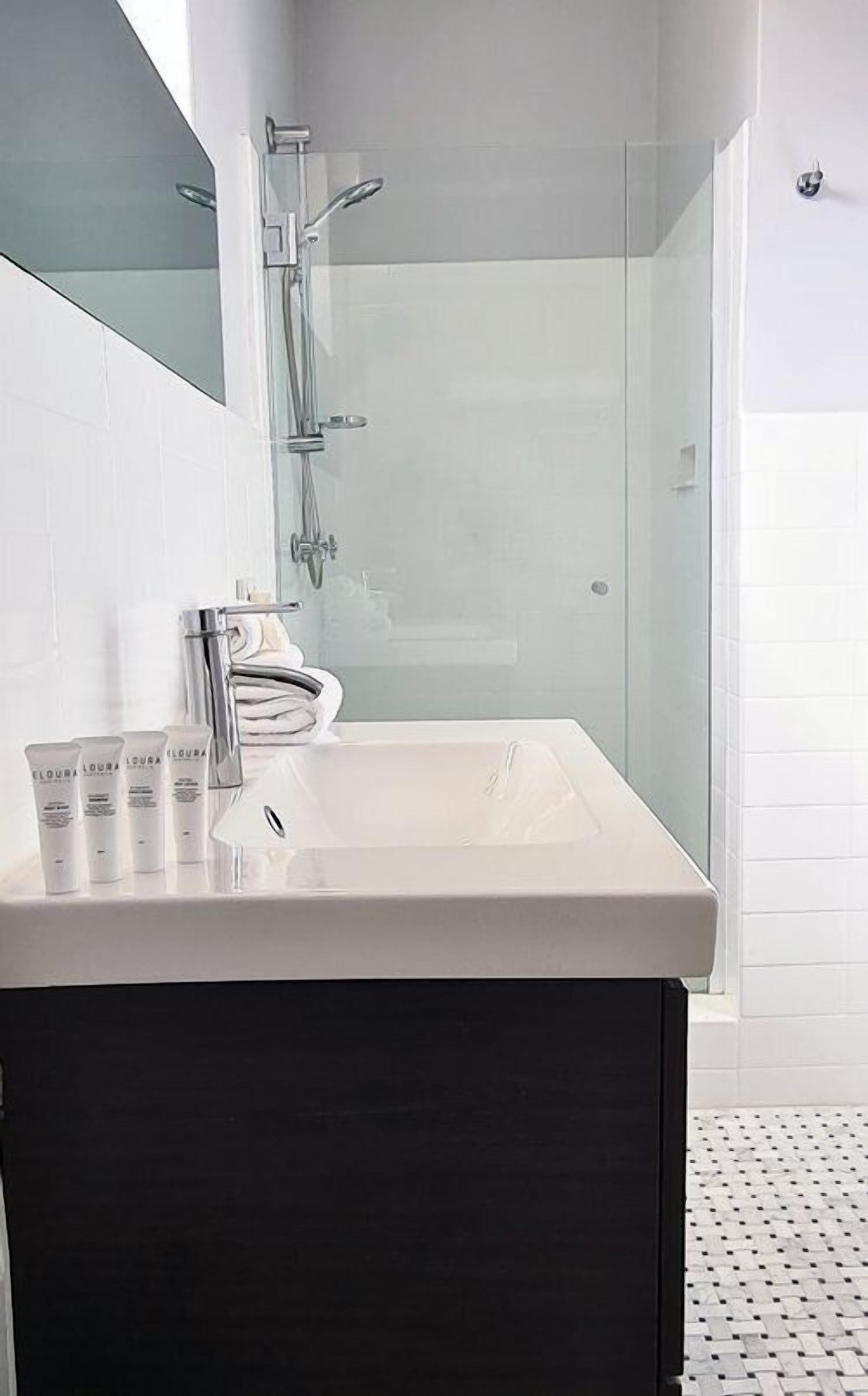 A modern bathroom with a white sink, glass shower enclosure, and a dark cabinet.
