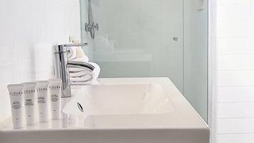A modern bathroom with a white sink, glass shower enclosure, and a dark cabinet.