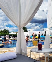 Un área de piscina con toldos blancos, sillas de descanso y una mesa con bebidas.