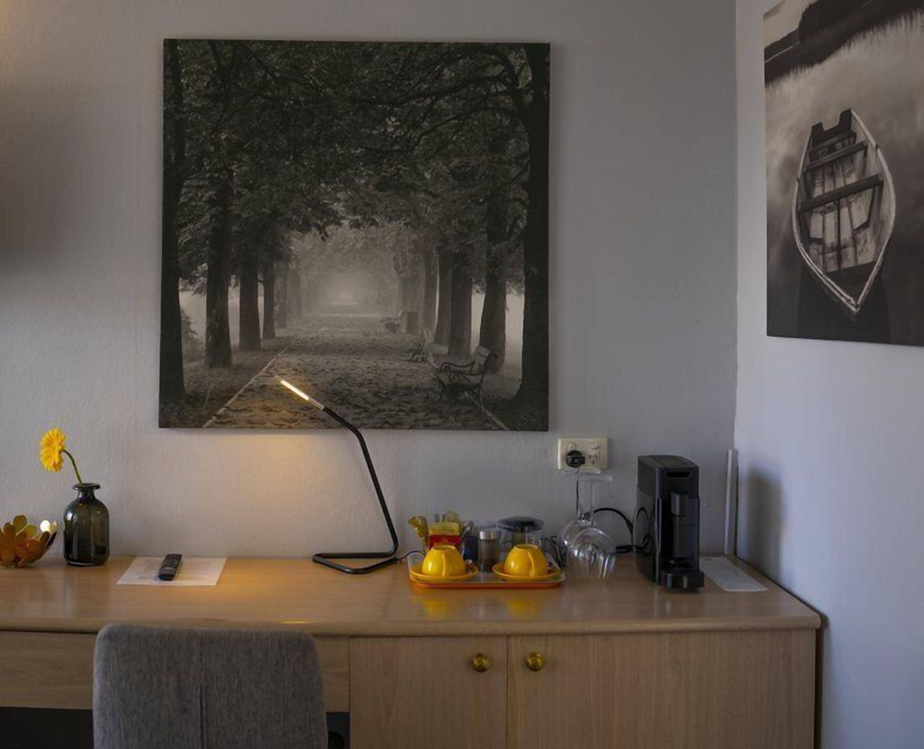 A desk with a lamp, a vase with flowers, a coffee maker, and a remote control.