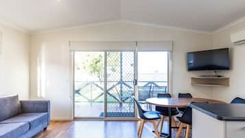 Ein modernes Wohnzimmer mit einer Couch, einem Esstisch mit Stühlen, einem an der Wand befestigten Fernseher und einer Glasschiebetür zu einem Außenbereich.