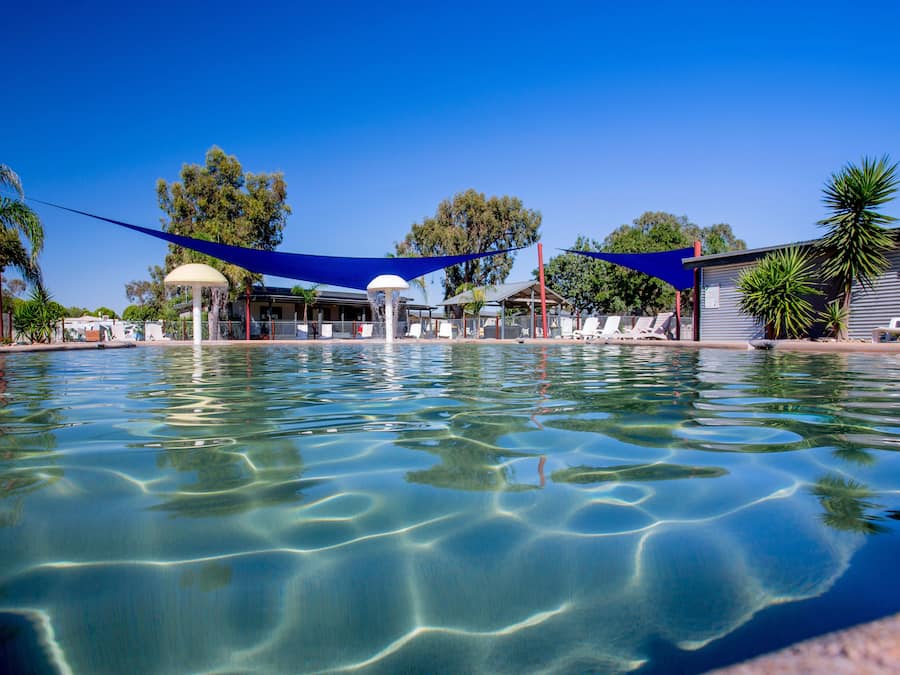 Piscina límpida com toldo azul, espreguiçadeiras e um gazebo.