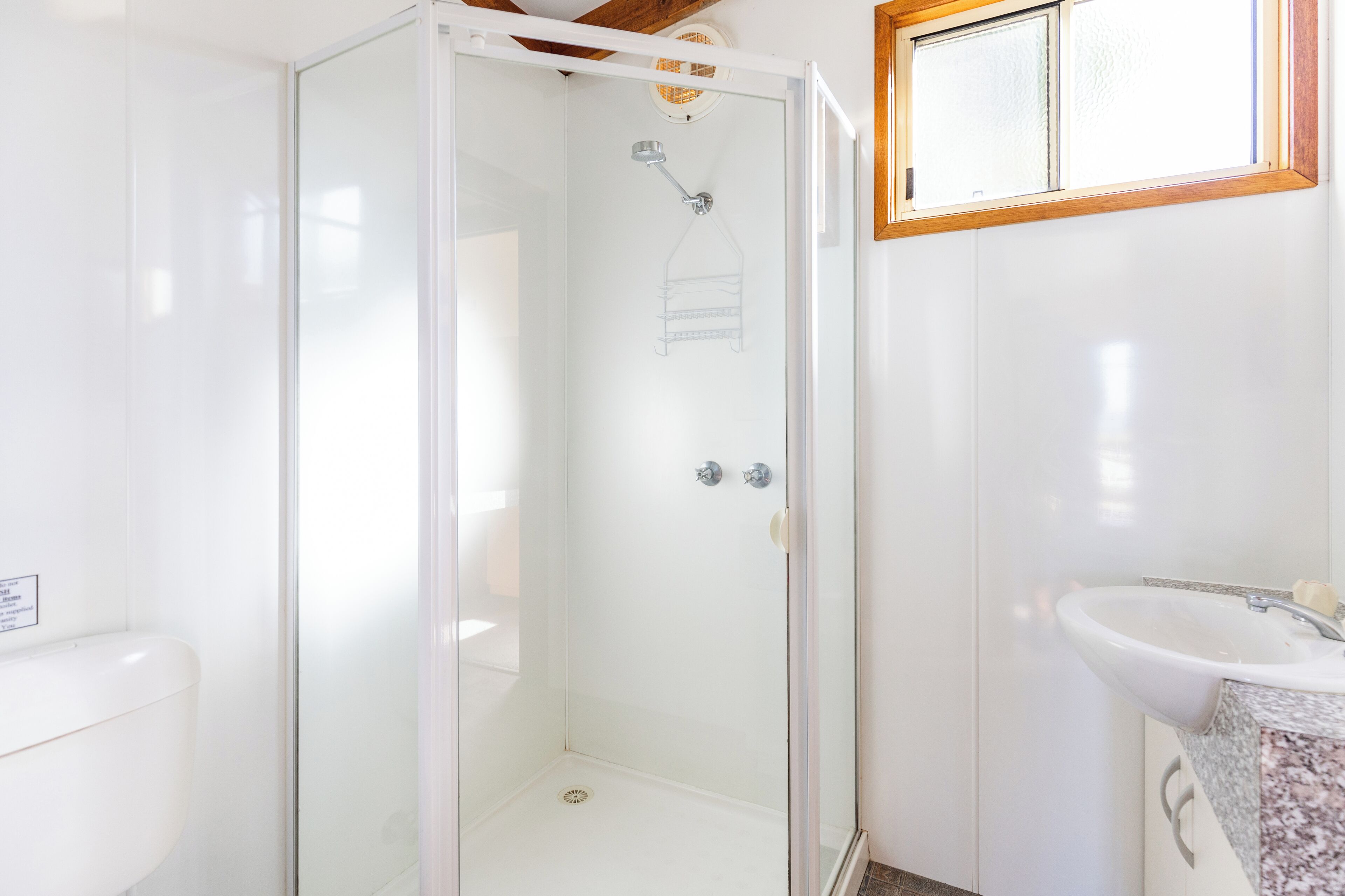 Ein modernes Badezimmer mit einer gläsernen Dusche, einem weißen Waschbecken und einer Arbeitsplatte aus Granit.